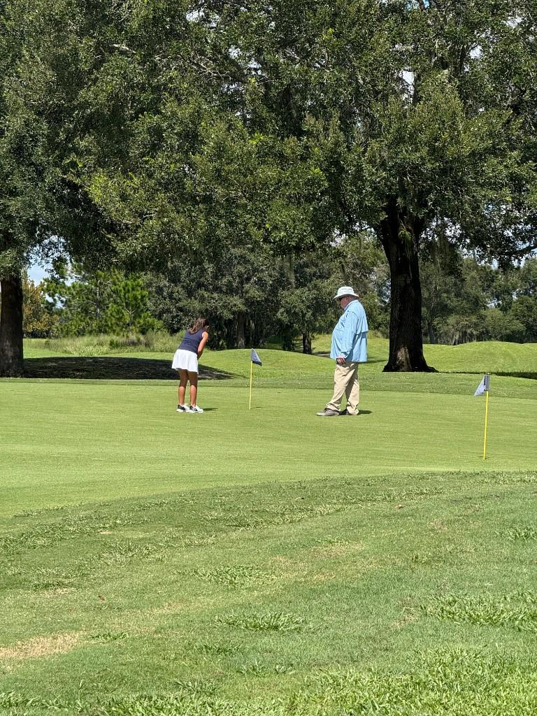 Practicing putting on a sunny green while a coach watches nearby.