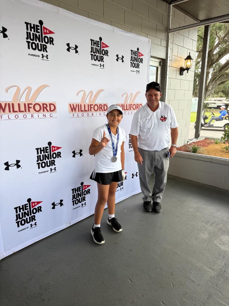Alex with a tournament medal, celebrating first place next to a coach at The Junior Tour